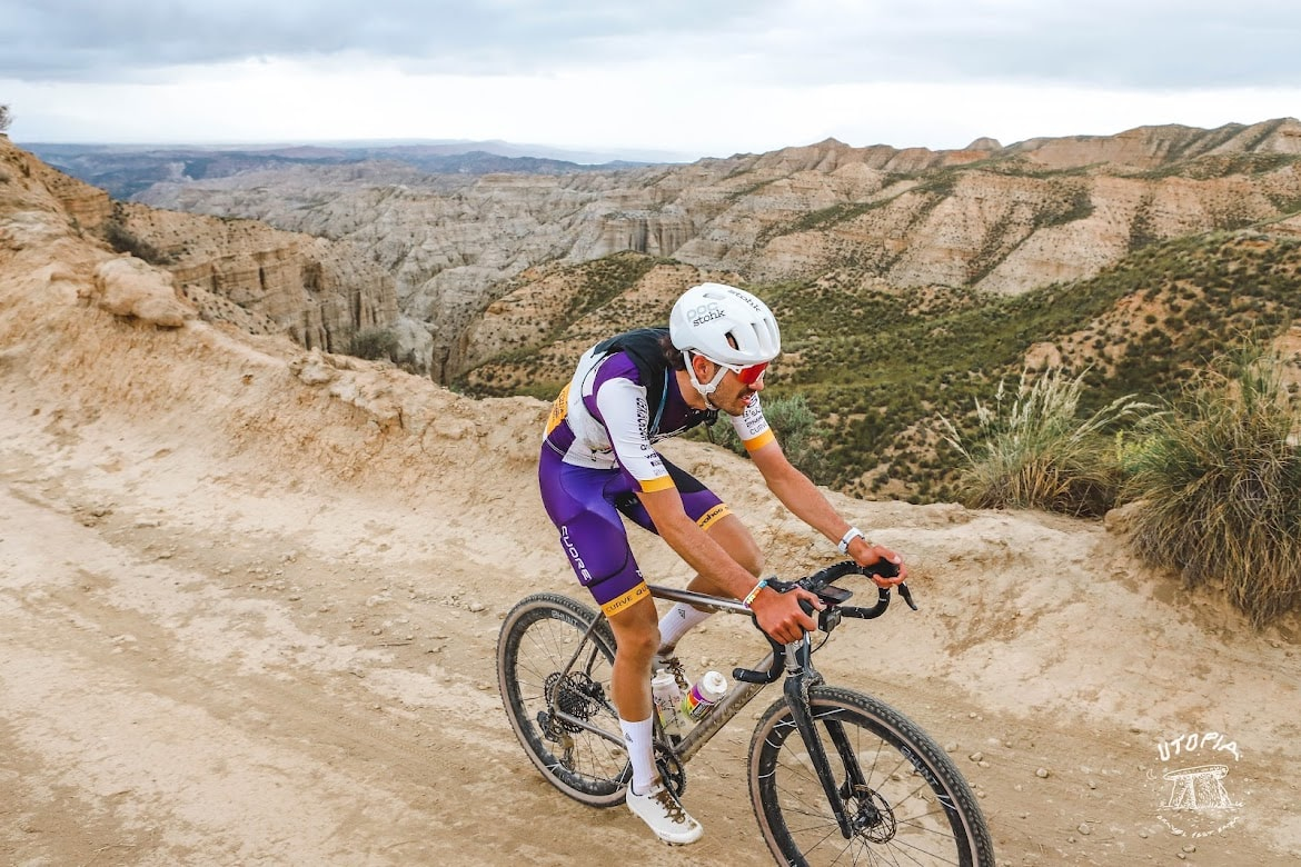 Man in full cycling kit cycling along a sandy road high in the hills