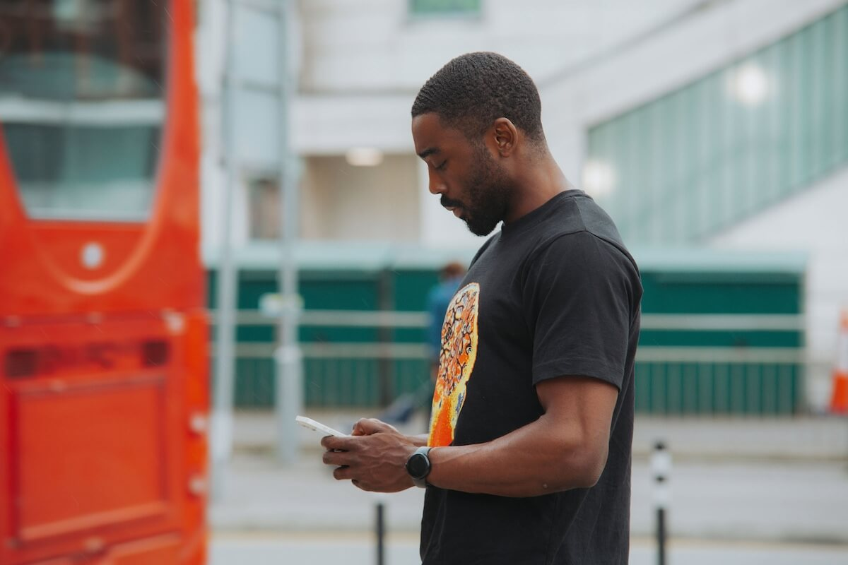 Man uses phone in street with red London bus in background