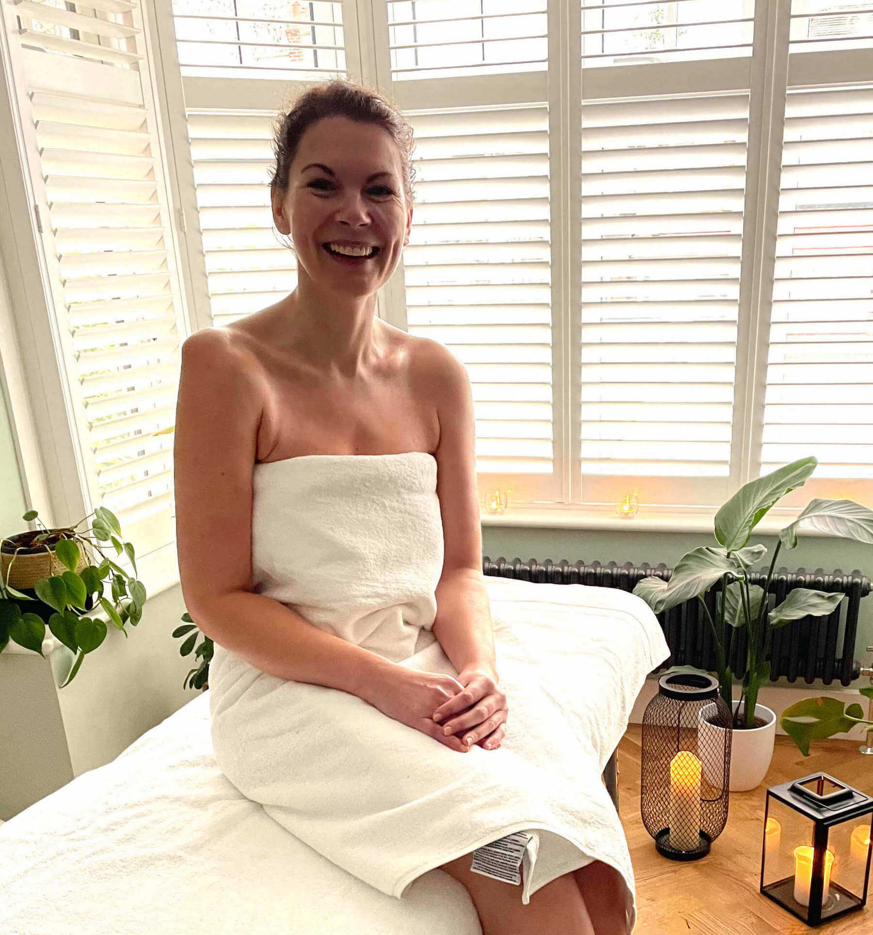 Woman smiles at camera sitting on massage table at home in London apartment