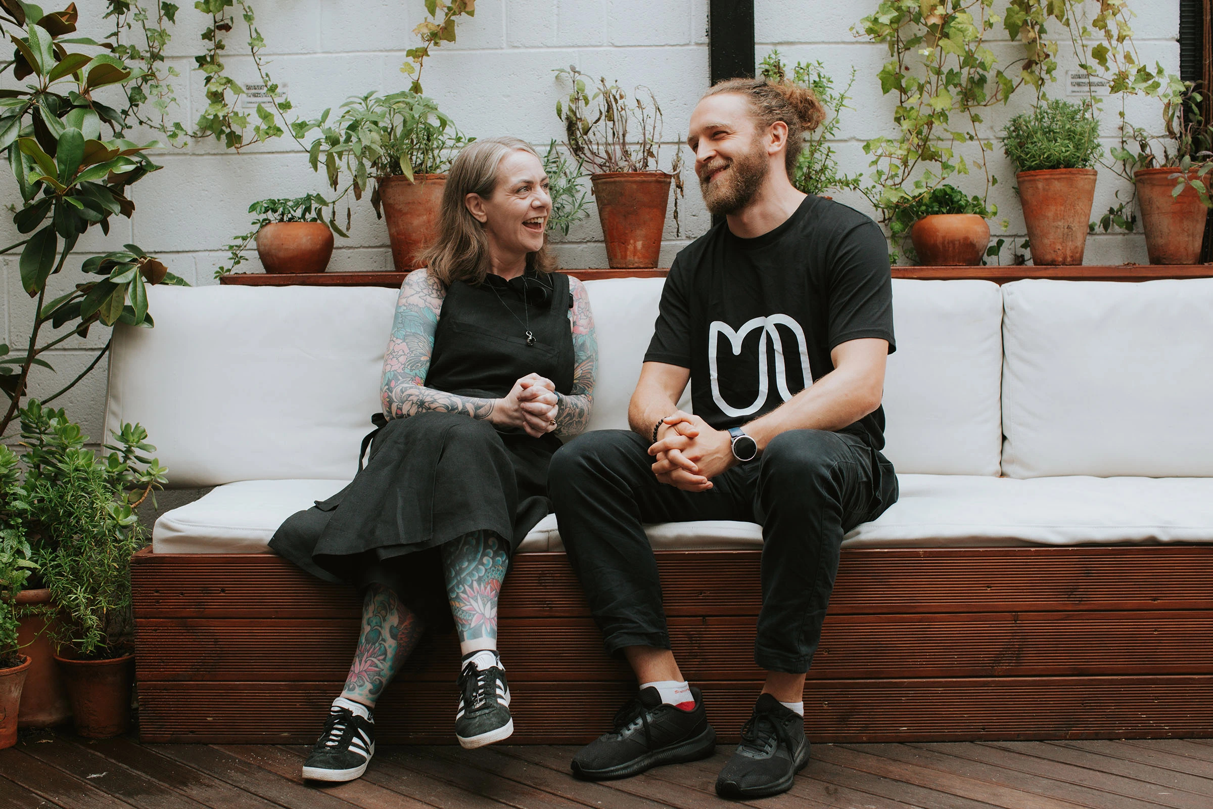 Artist Charlotte and Urban osteopath Fabio sitting together on a bench laughing