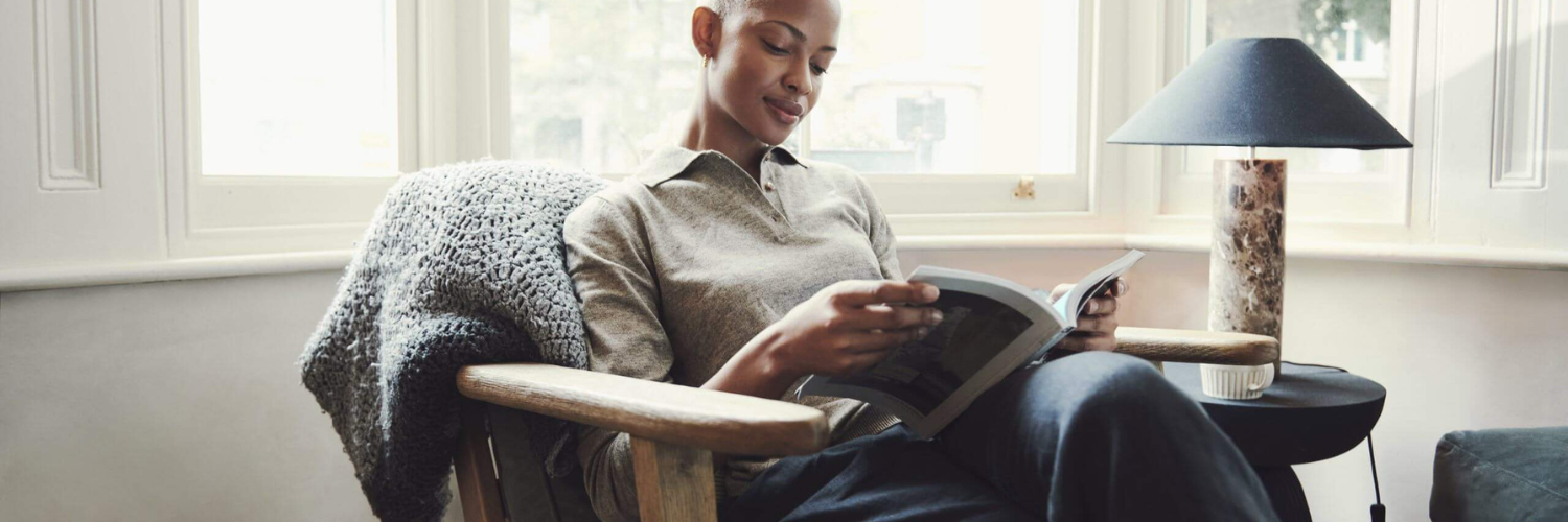 Woman sitting in a chair reading a book with a drink next to her