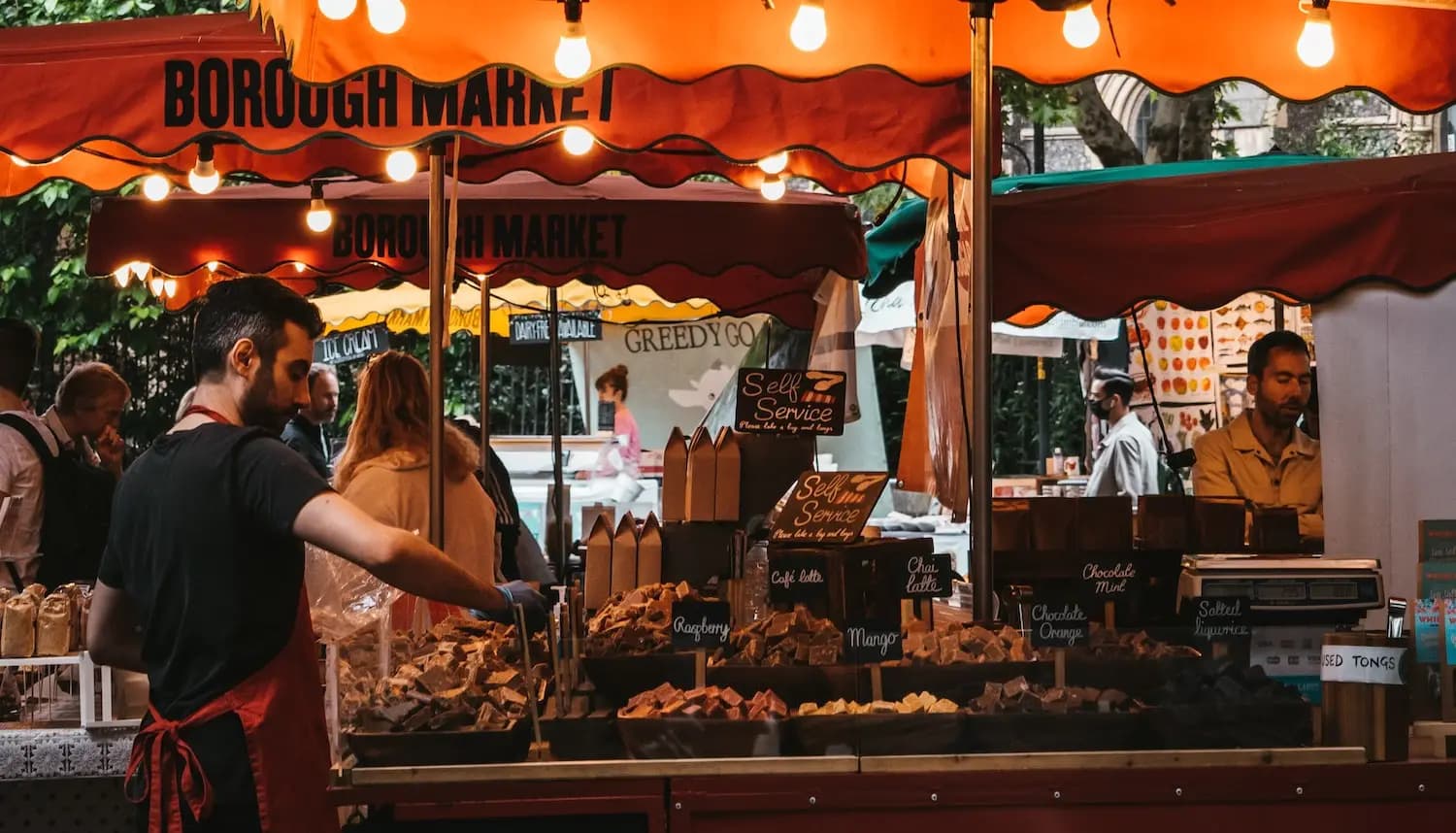 A market stall holder sets up food under festoon lights in Borough Market London