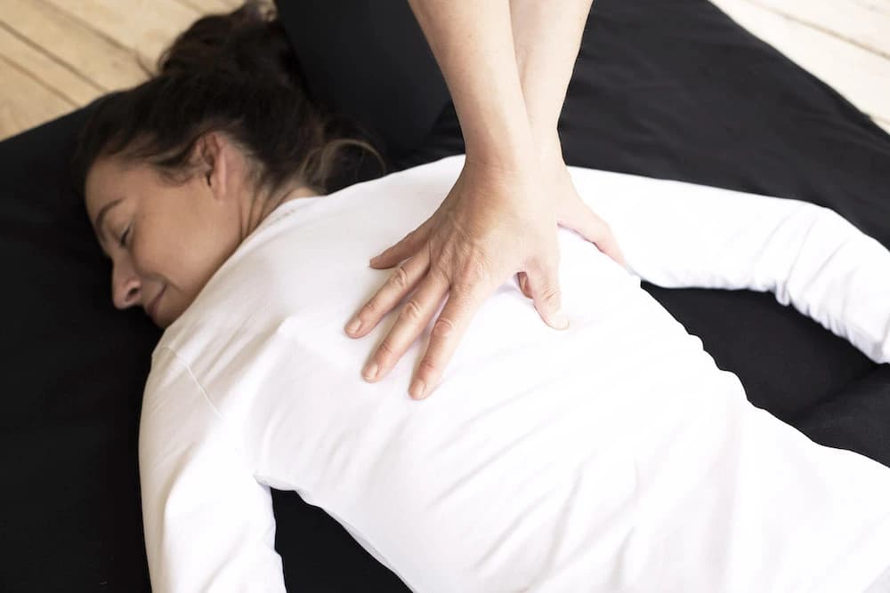 Client lies on her front on a yoga mat while therapist performs full body shiatsu massage