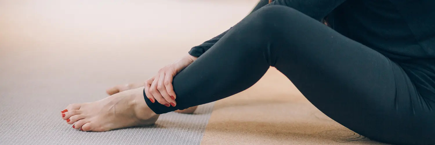 Woman in leggings sits on yoga mat trying to touch toes