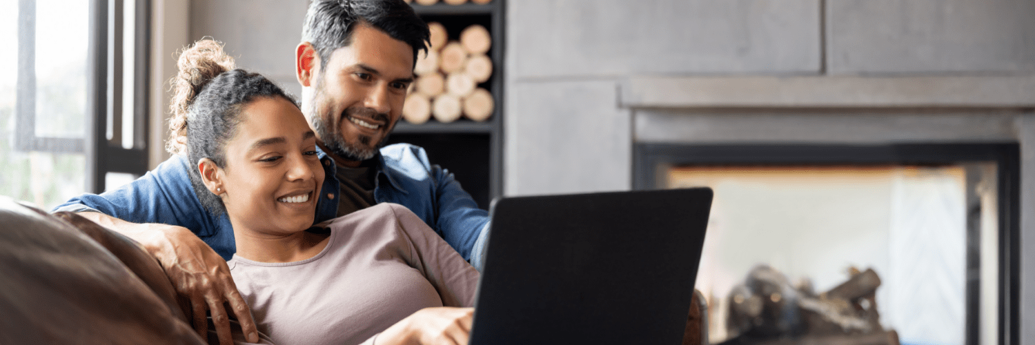Man and woman sitting close together looking happy at a laptop