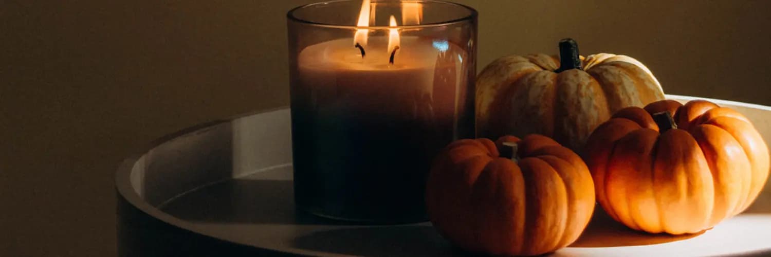 Lit candle with three small and medium pumpkins decorating a table