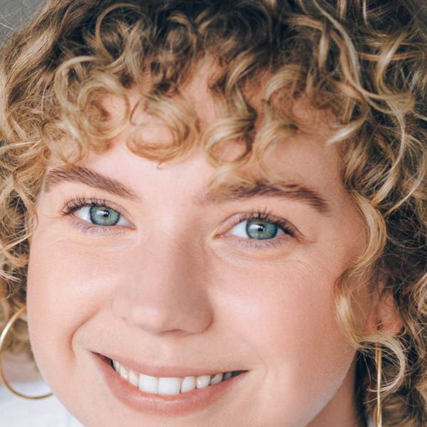 Smiling woman with blue eyes, curly blonde hair and gold earings