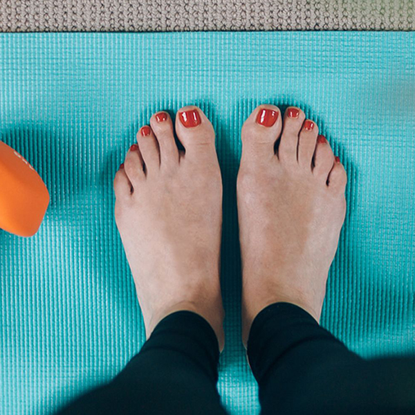 Pedicured feet with red nails on blue yoga mat