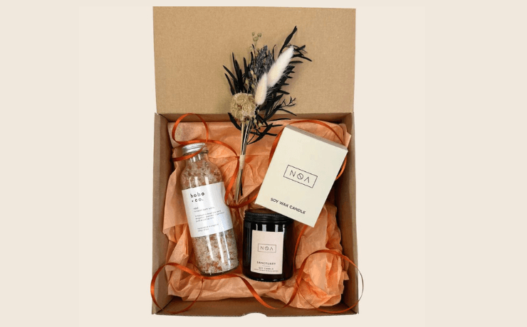A gift box containing bath salts, a candle, orange tissue paper and dried flowers