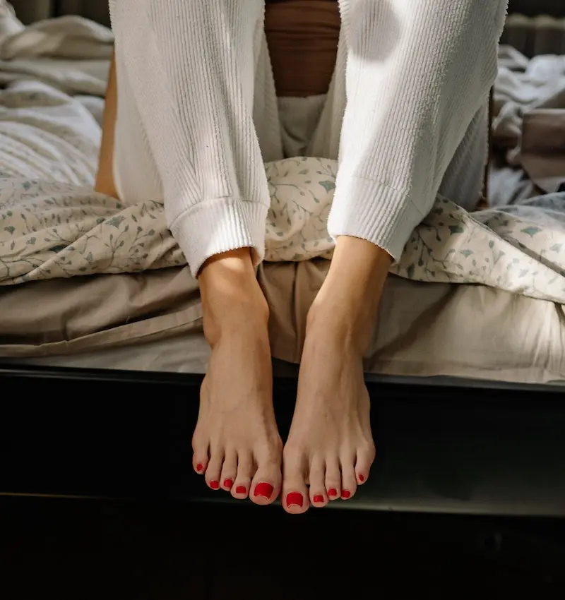 Model with red painted toenails sitting on bed in London apartment