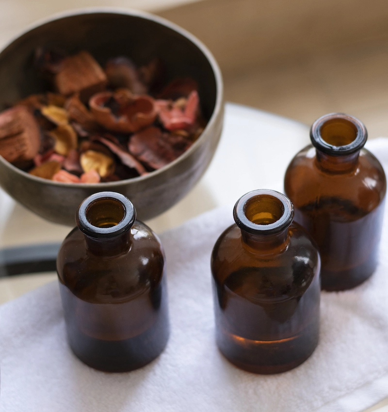 Apothecary massage oil bottles on a towel next to a bowl of pot pourri